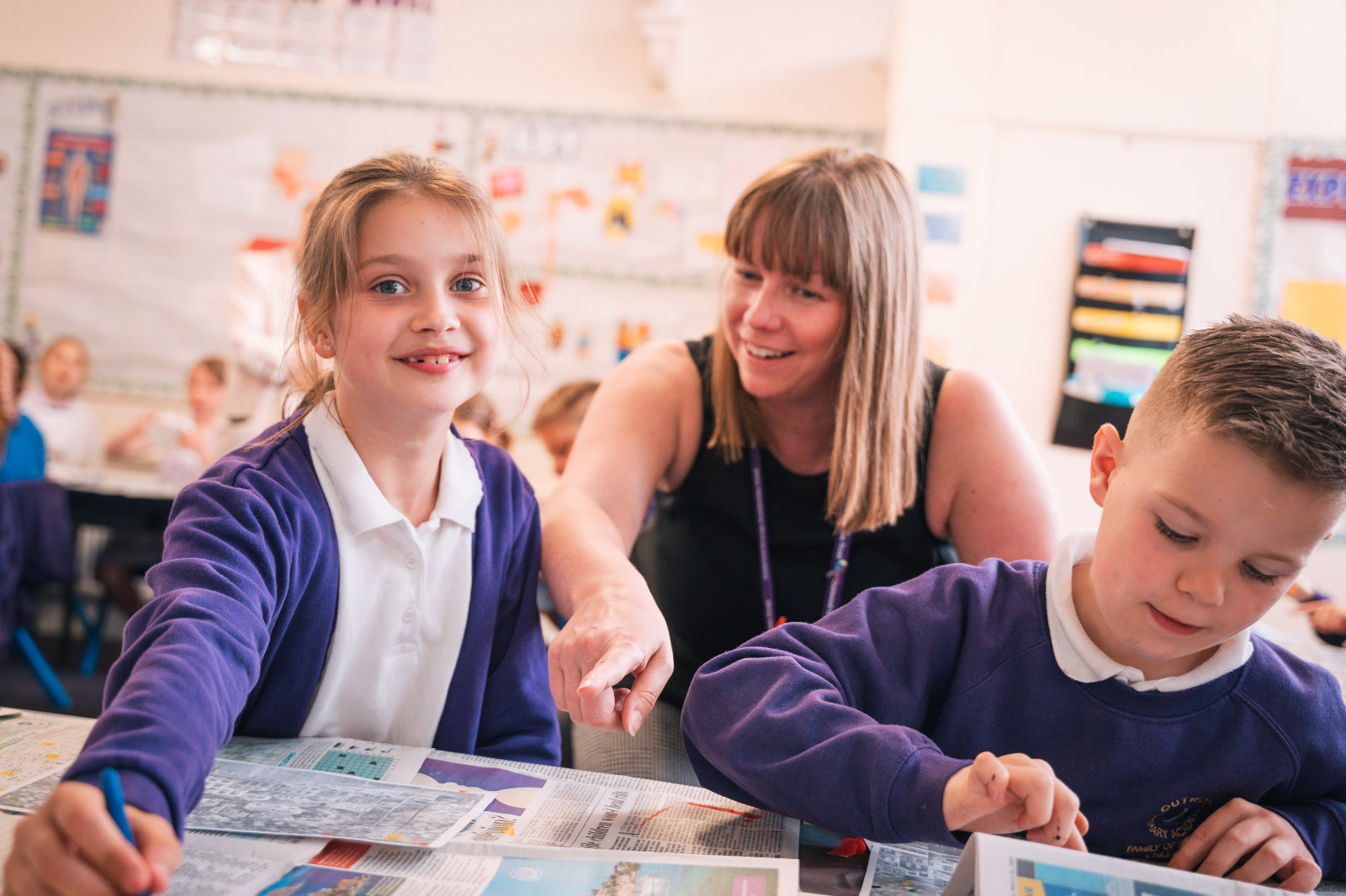 Two primary school children painting, with a teacher behind them pointing to their work